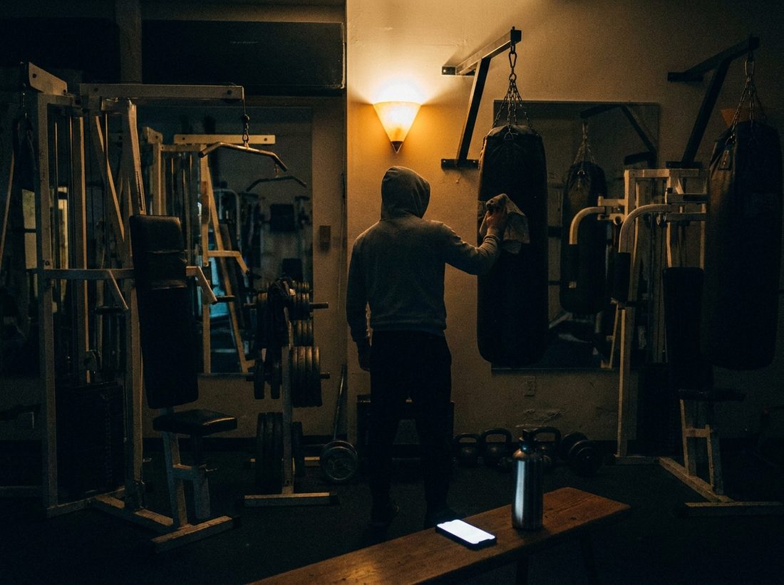 A boxing gym at night, a coach wiping down a bag under a wall light